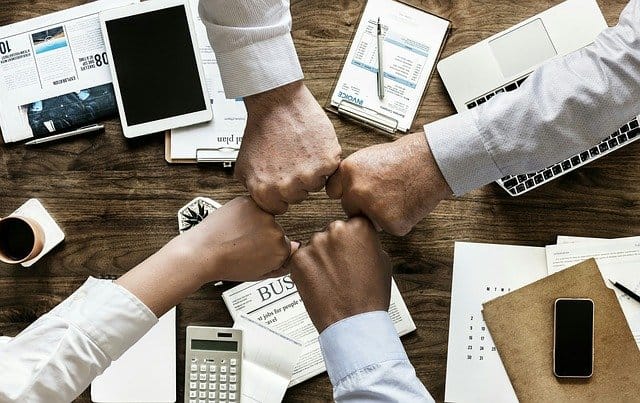 Four hands give a fist bump above a desk covered in business materials