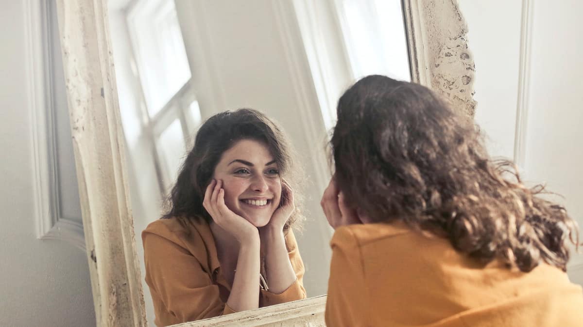 Person leaning close to mirror smiles at their reflection